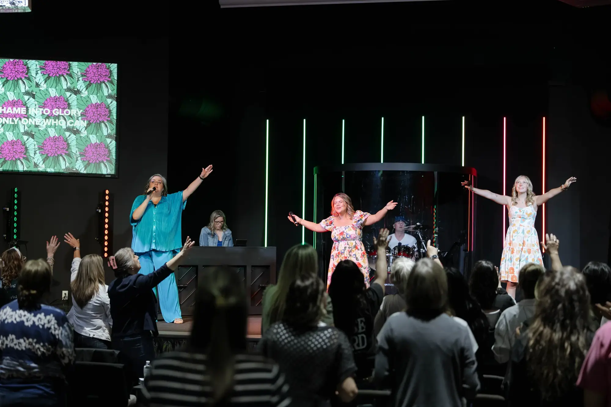 Women leading worship on stage with their arms raised at a Crowned night