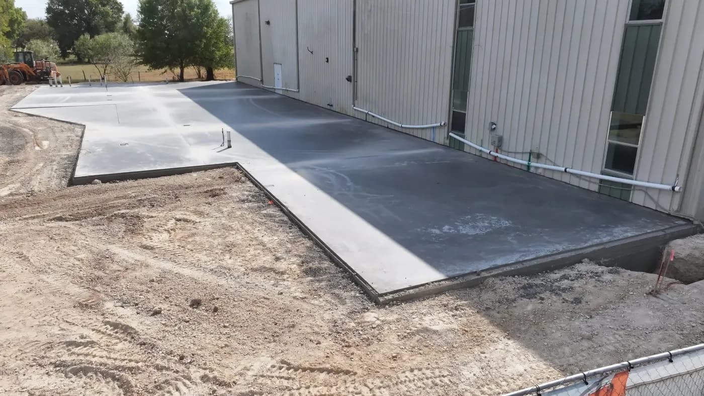 A freshly poured concrete slab runs along the side of the metal church building