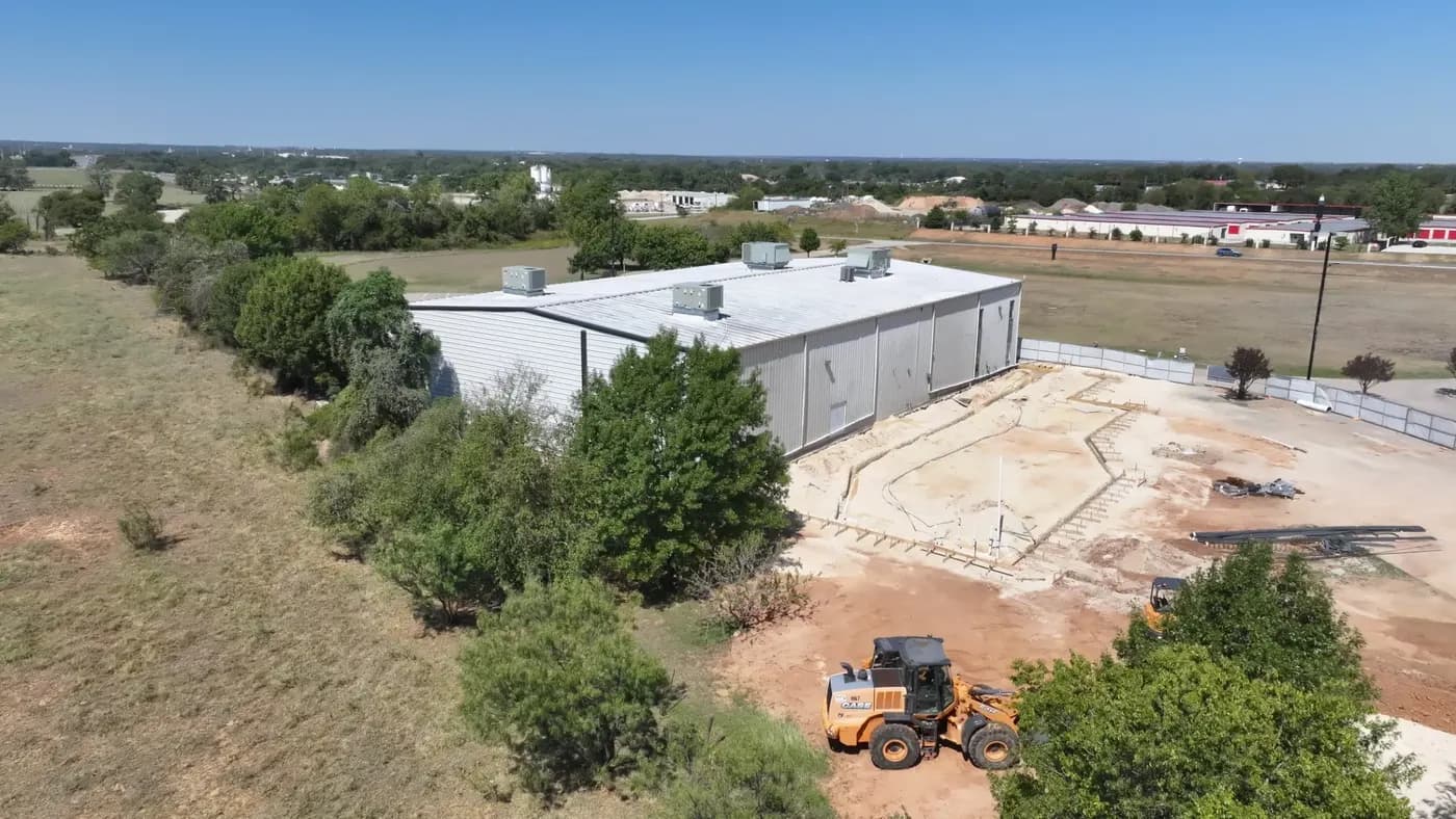 A loader sits on the graded dirt behind the Belton building, with forms laid out for new construction