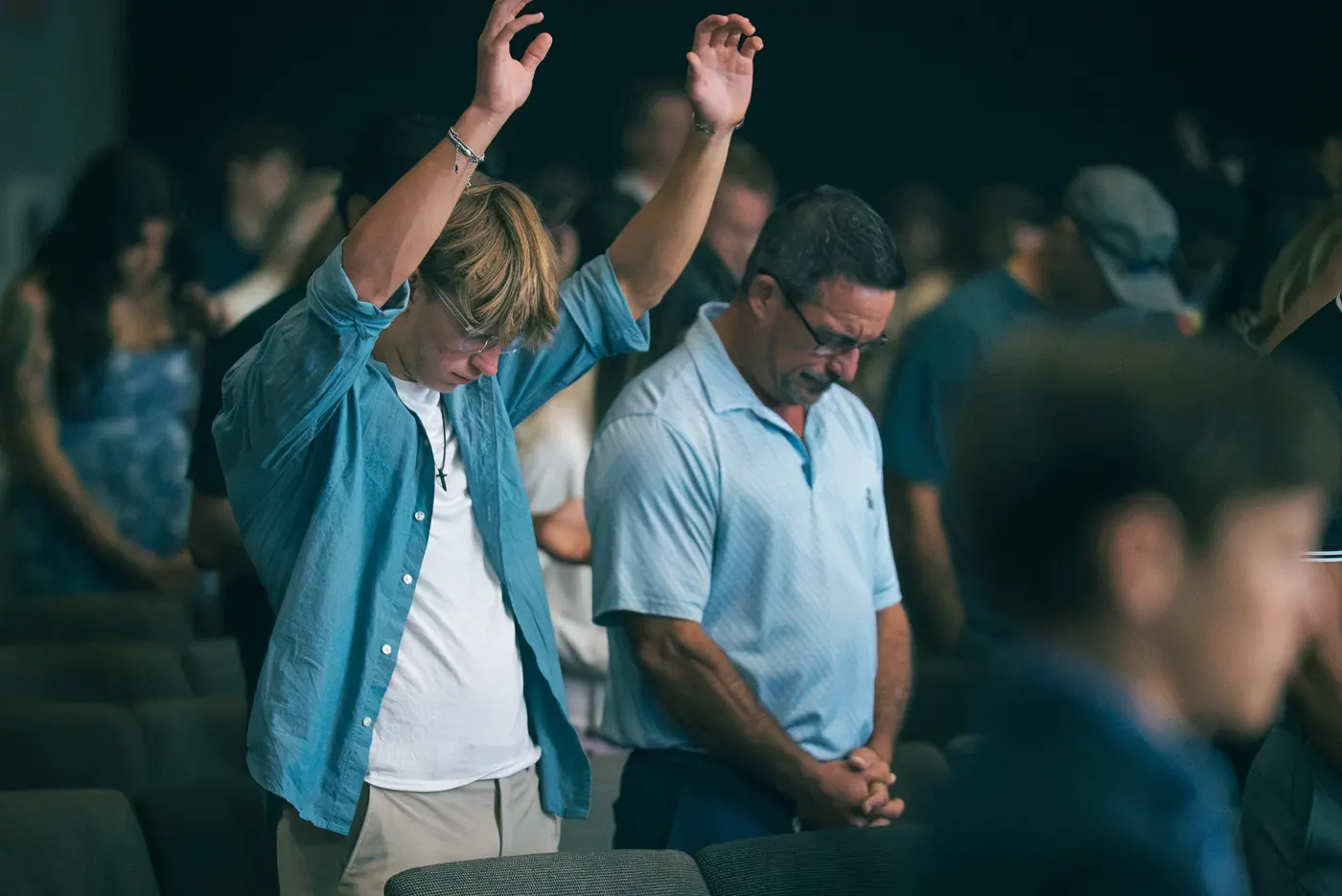 Two men in worship during a Sunday service, one with hands raised, one with head bowed
