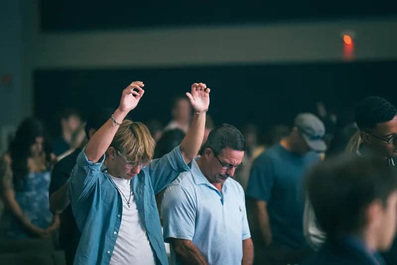 A Sunday service at Harker Heights, one worshipper with both hands raised beside another with head bowed