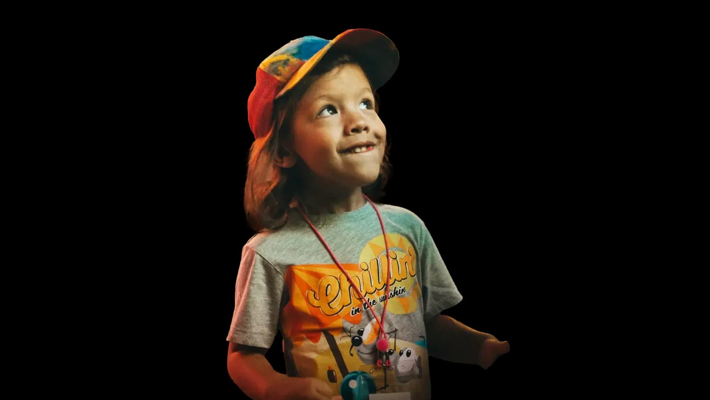 A young child in a bright patchwork cap grins and looks up