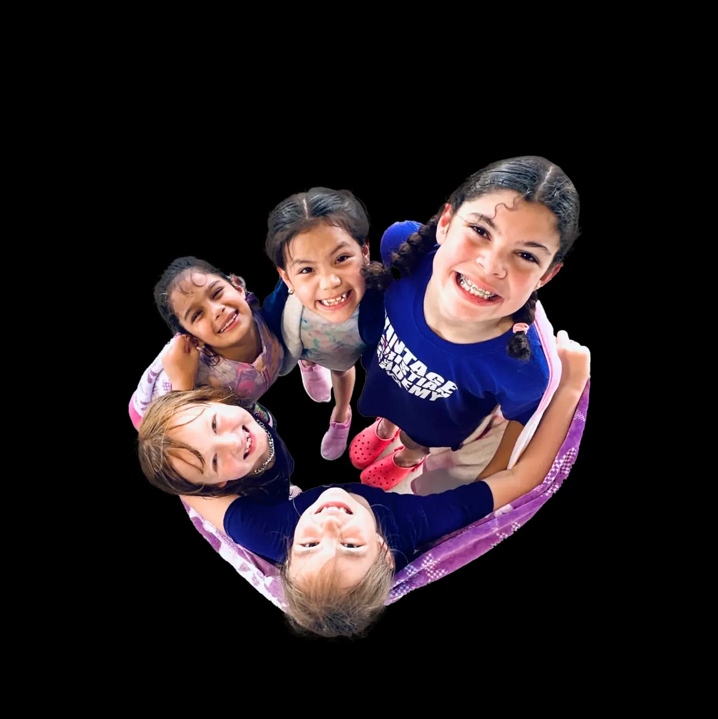 Five girls stand in a circle and grin up at the camera from above