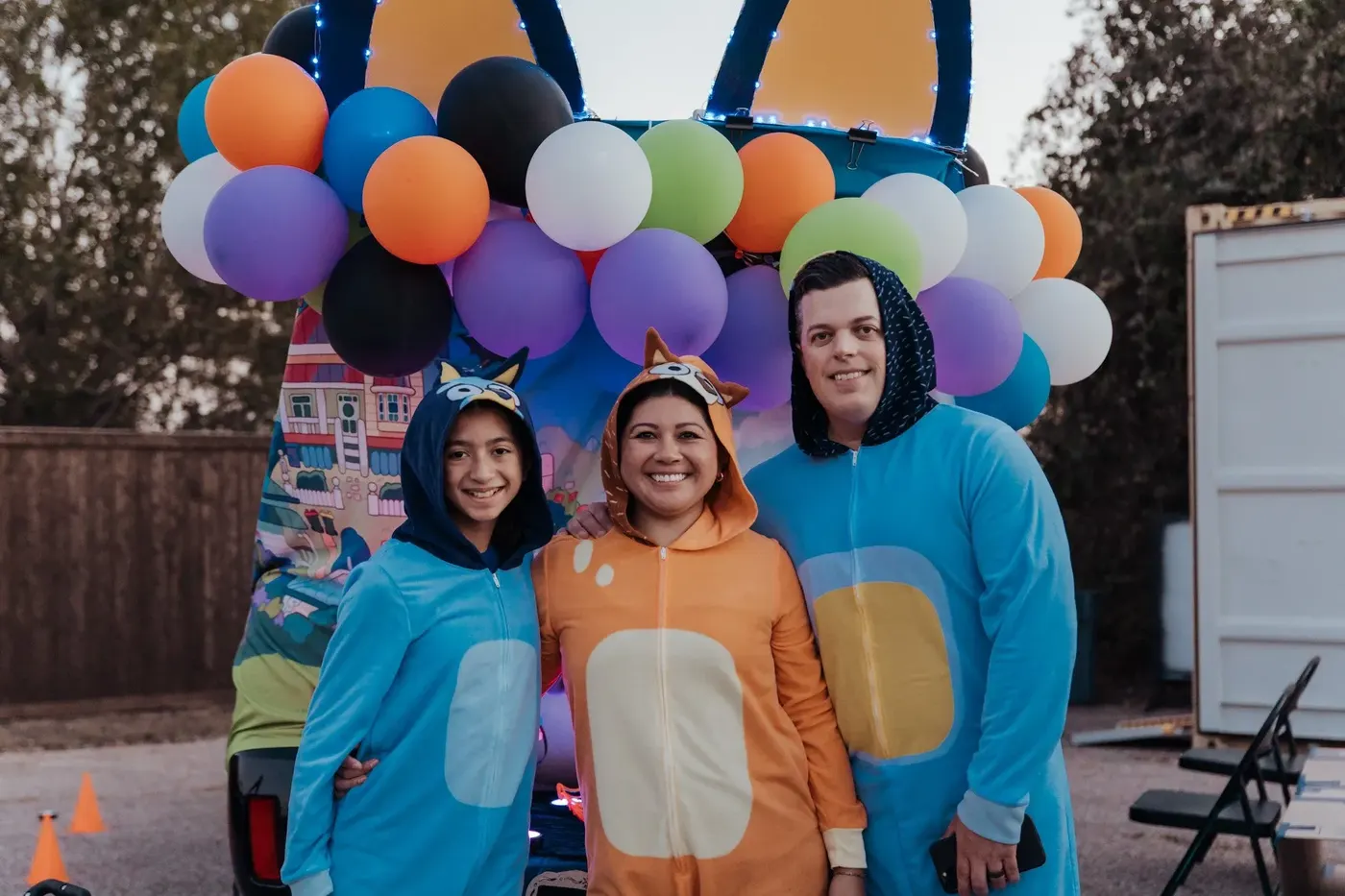 Three volunteers dressed as Bluey characters in front of a balloon-covered trunk