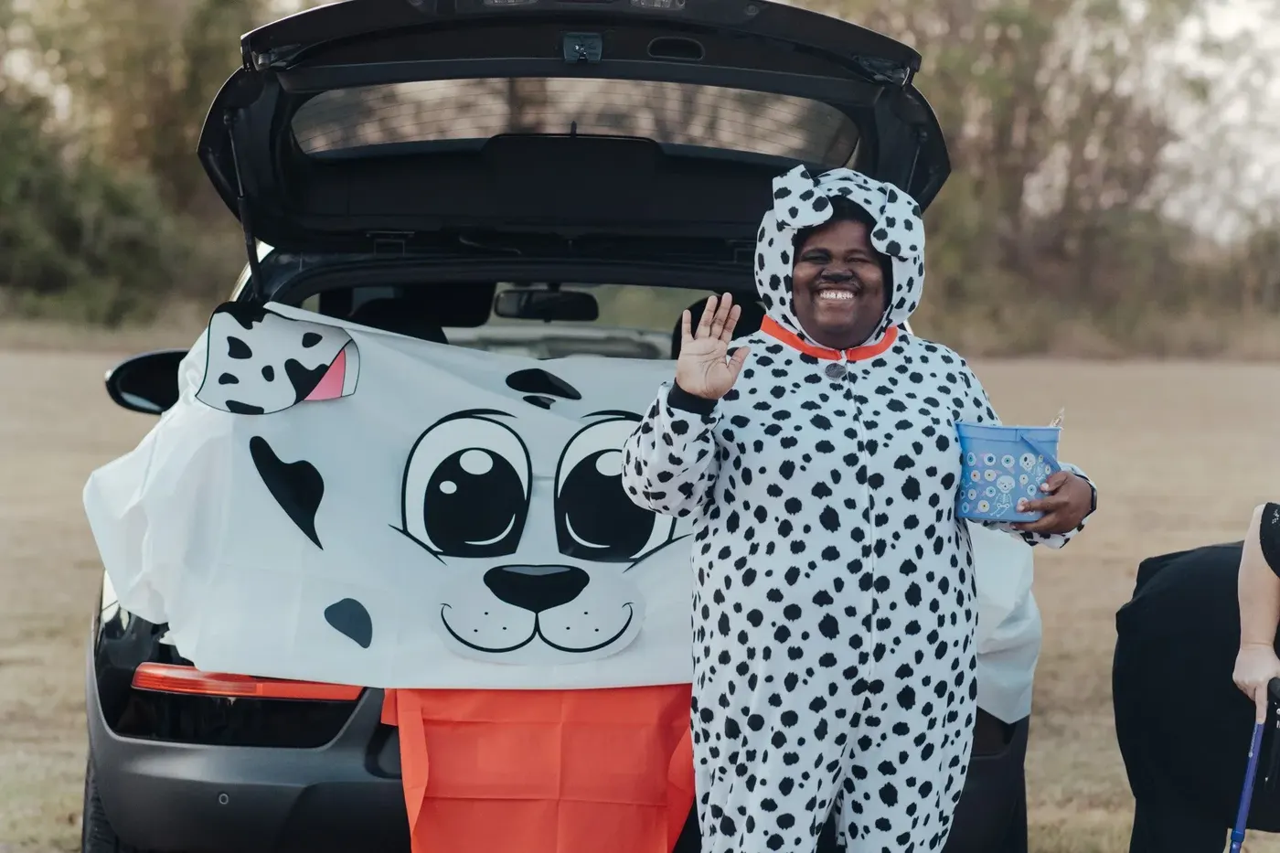 A volunteer in a Dalmatian costume waves beside a car decorated as a puppy