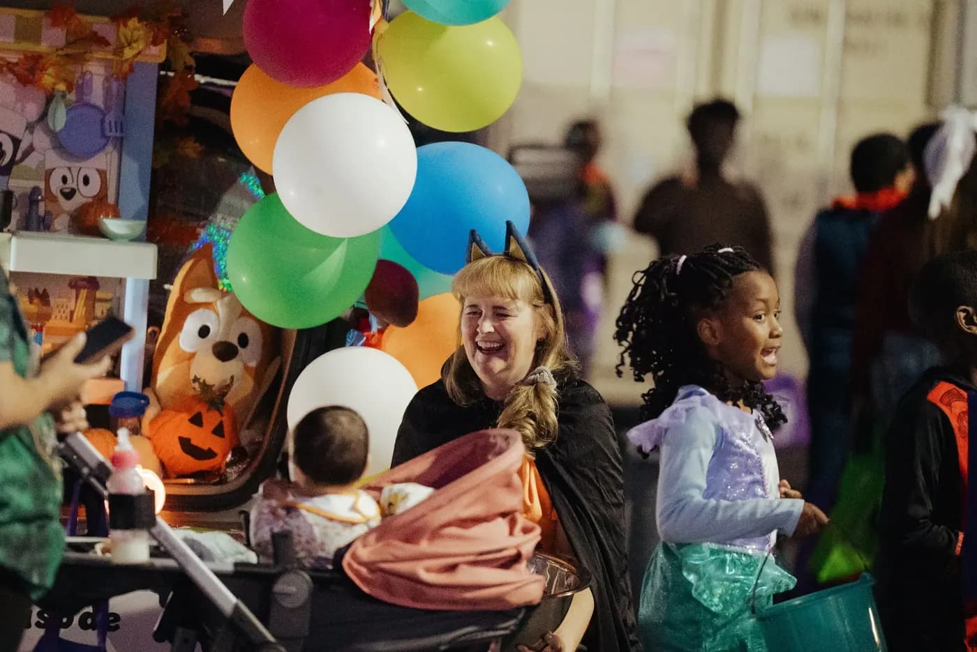 A volunteer in a cat-ear headband laughs beside a trunk decorated with balloons