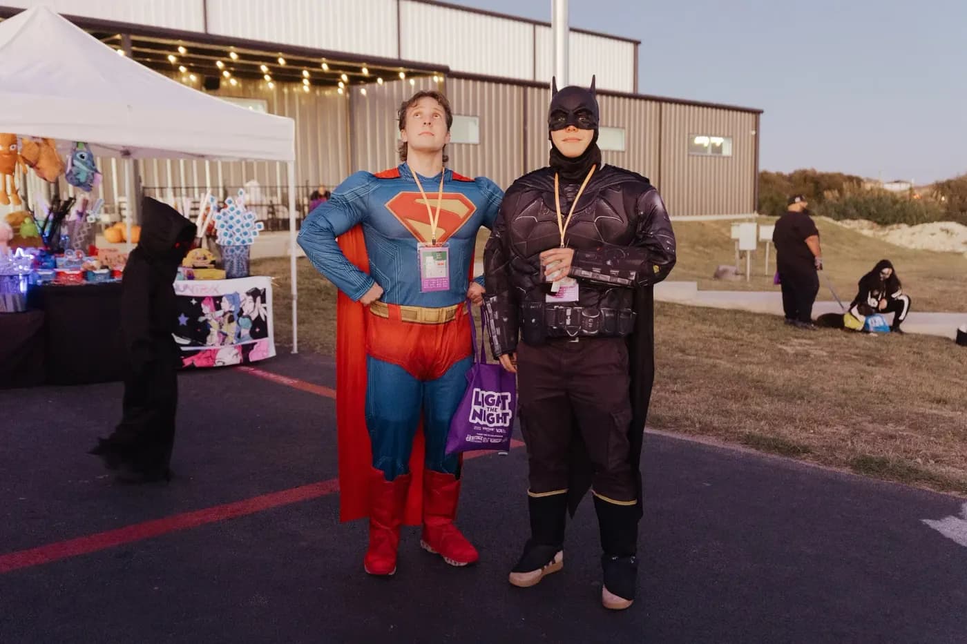 Two volunteers dressed as Superman and Batman stand by the booths at dusk