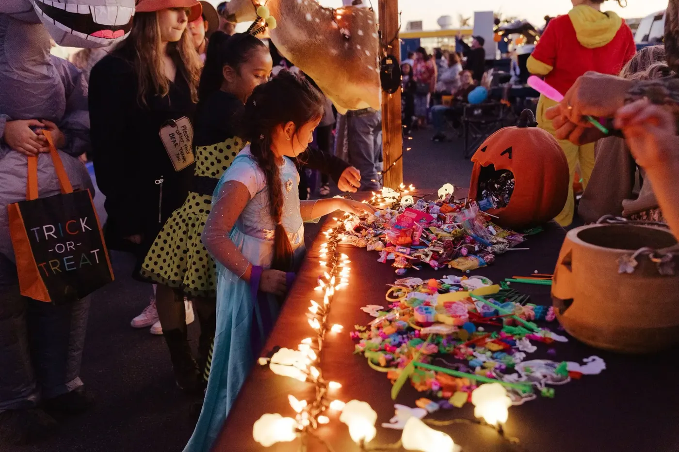 Children in costume choose candy from a table lit with string lights