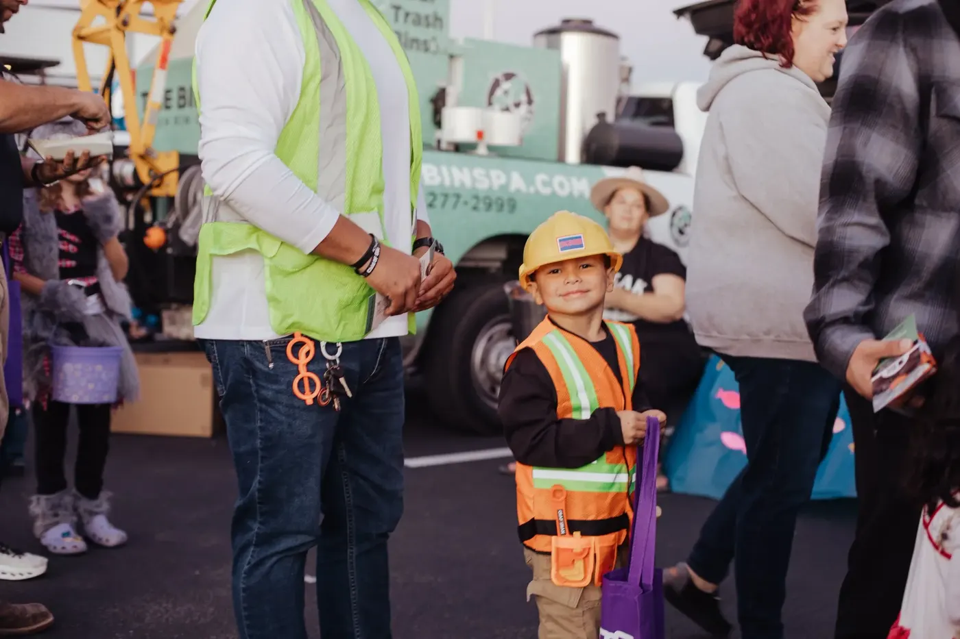 A small boy in a hard hat and safety vest trick-or-treats among the crowd